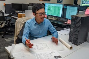 A recent grad, smiling at his desk and enjoying his work because he did his research into the best types of architecture jobs for California graduates.