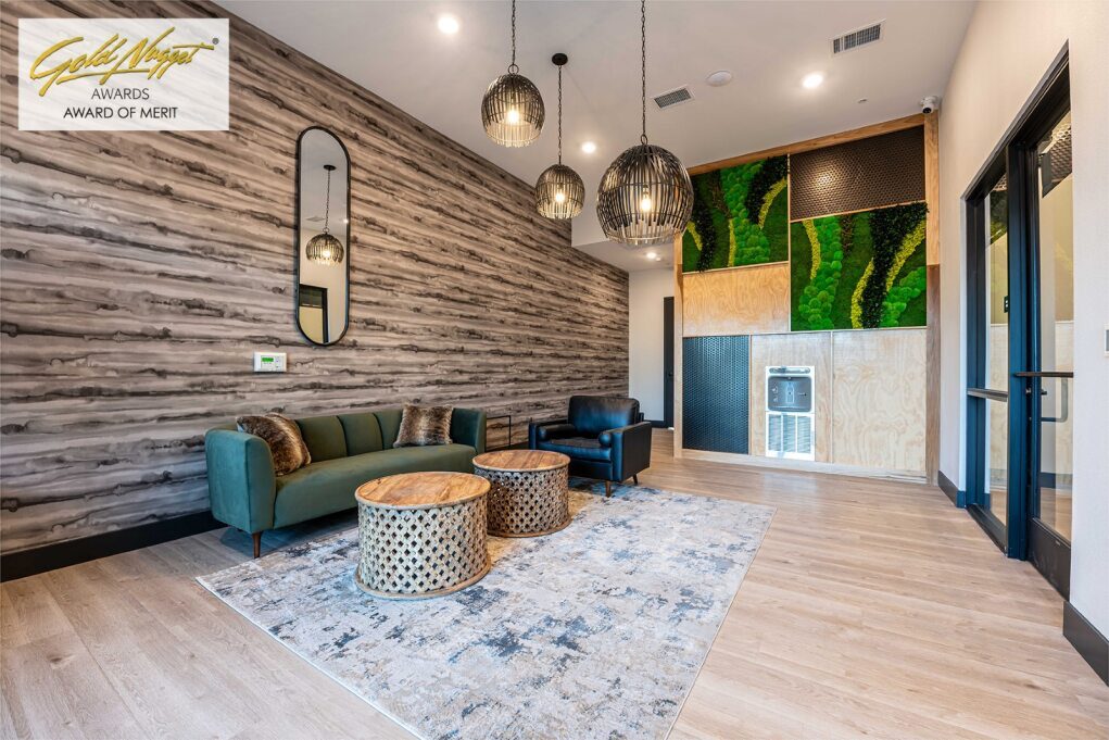 A modern lounge area with a green couch, black armchair, round coffee tables, and a rug. Decorative wooden wall on the left, green vertical garden wall on the right, and three hanging light fixtures—an interior worthy of awards of merit at Golden Nugget.