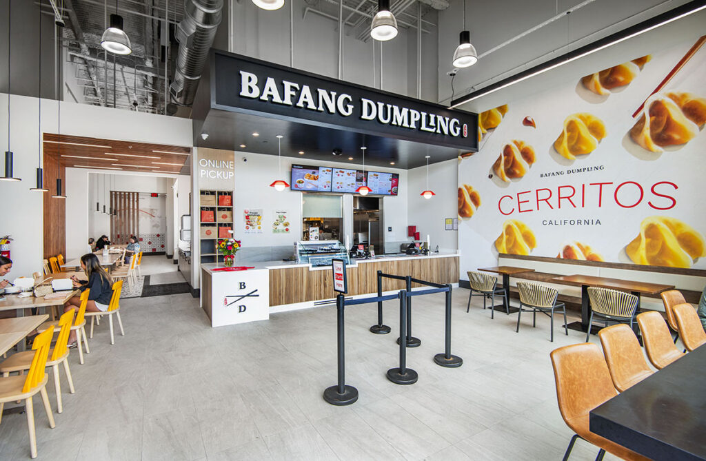 Interior of BaFang Dumpling restaurant in Cerritos, California, showing the ordering counter, seating area, and large wall graphics depicting dumplings.