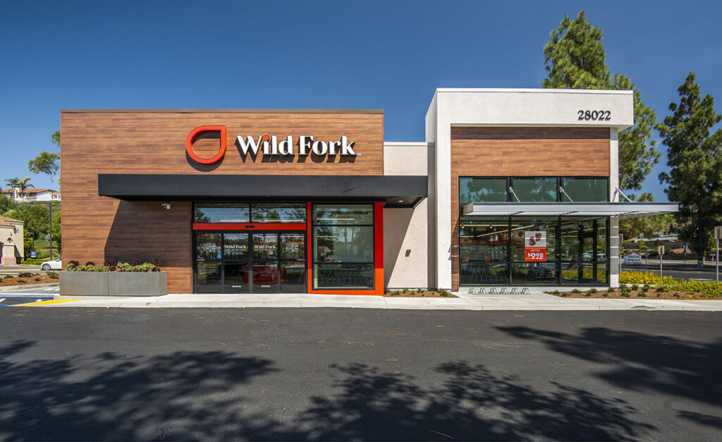 A modern storefront of Wild Fork, featuring a combination of wood and white exterior with the store's logo prominently displayed.