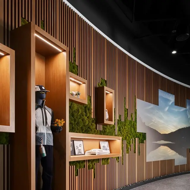 Subaru design studio in Tustin, California, with a curved wood-slat feature wall, preserved moss, recessed display niches, and a mannequin in branded apparel