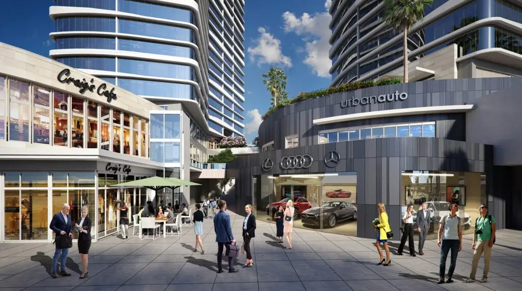 Street-level plaza at a mixed-use development with a cafe terrace, an auto showroom for Lexus, Audi, and Mercedes-Benz, and residential towers above