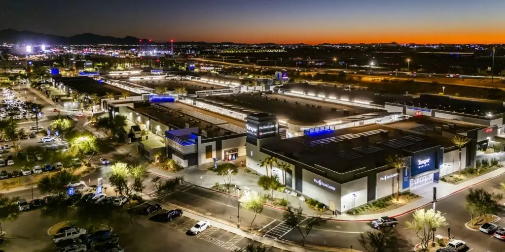 Tanger Outlets in Glendale, Arizona, photographed at dusk with illuminated storefronts, palm trees, and the surrounding desert landscape