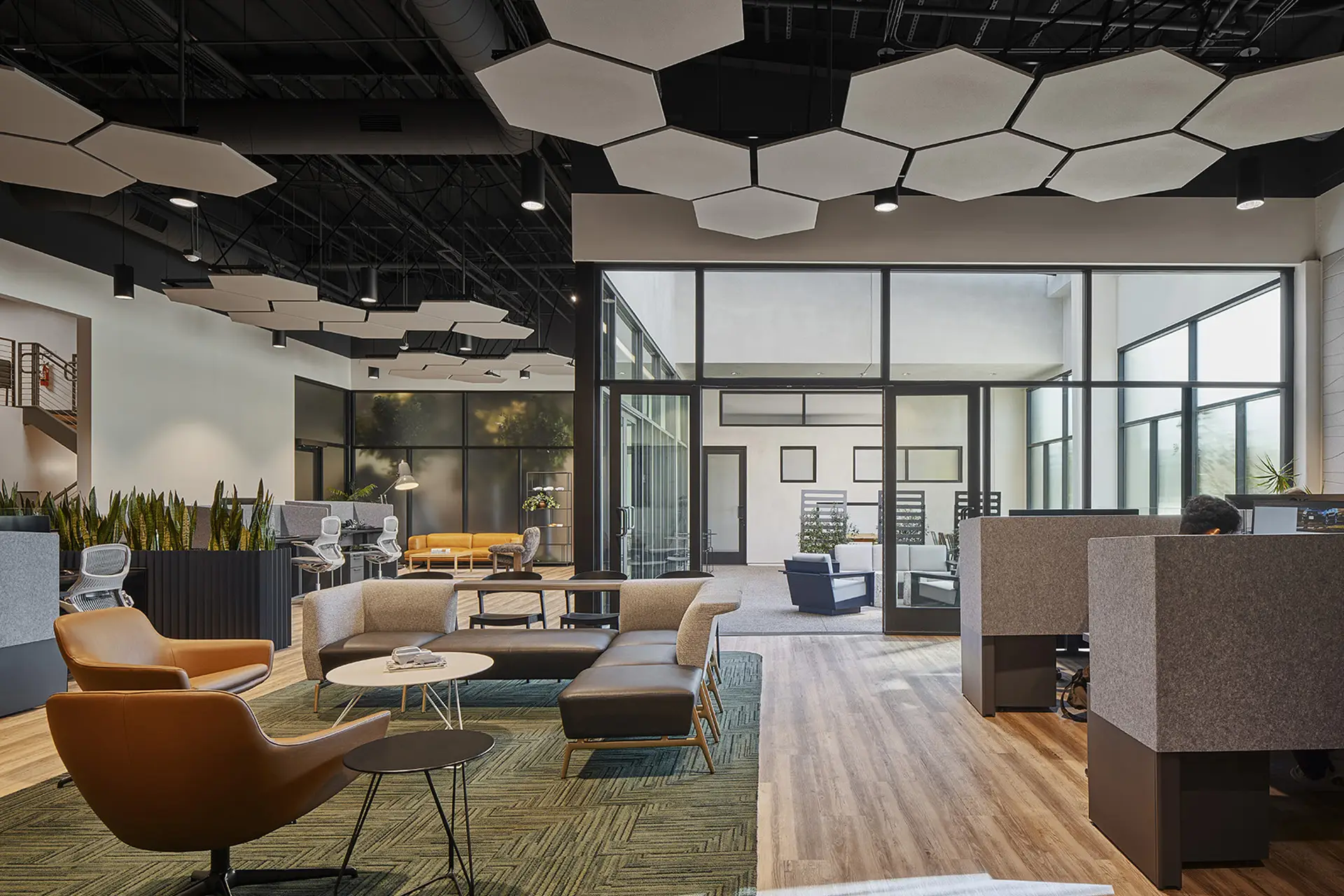 Open workplace lounge at North American Subaru R&D in Tustin, with hexagonal ceiling panels, seating, and glass-enclosed collaboration rooms