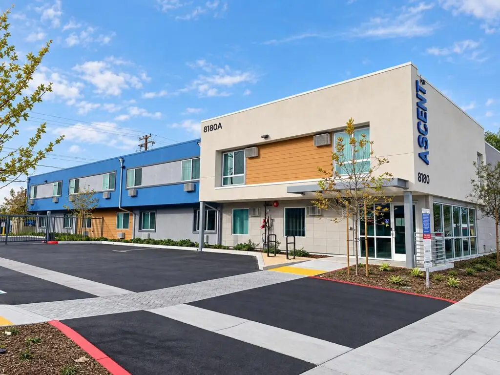 Ascent permanent supportive housing community in Buena Park with renovated two-story buildings, modern blue and neutral facades, and landscaped entry court