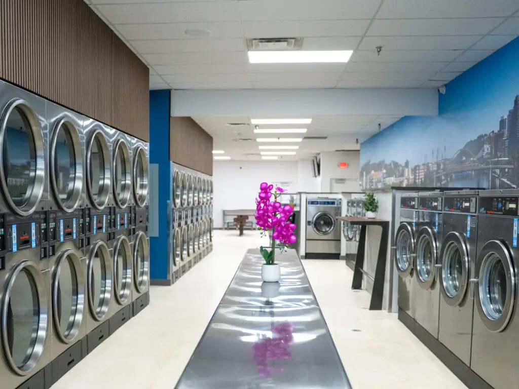 Interior of Suds in the City in Greensburg with rows of commercial laundry equipment and central folding table, designed by Architecture Design Collaborative.
