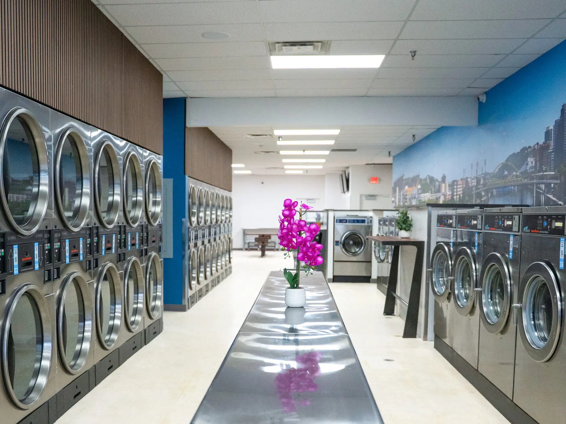Interior of Suds in the City in Greensburg with rows of commercial laundry equipment and central folding table, designed by Architecture Design Collaborative.