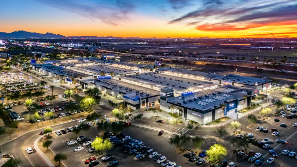 Aerial dusk view of Tanger Outlets Phoenix in Glendale, with renovated storefronts, parking, and desert mountains beyond