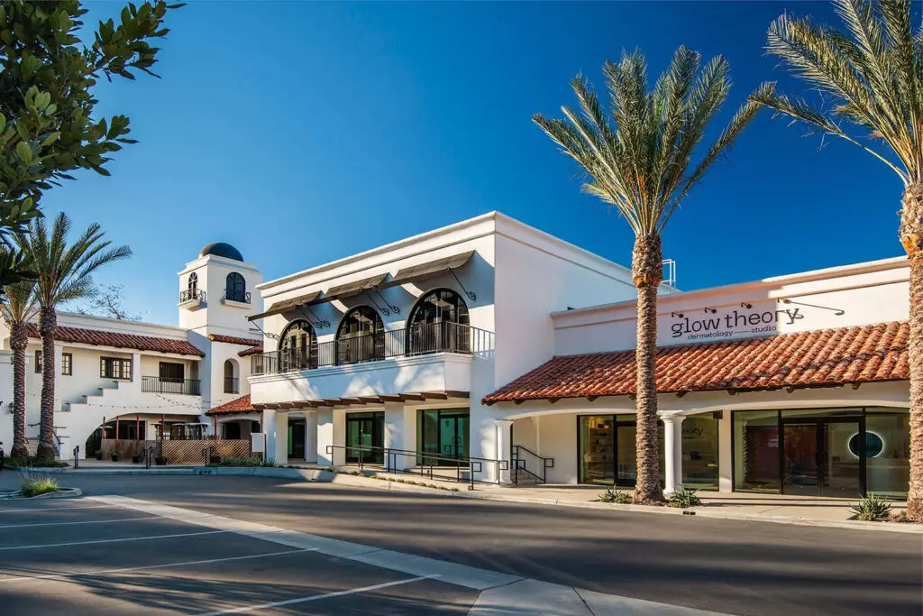 Street facade at The Beacon in Carlsbad, with a tower, arched balconies, tile roofs, and Glow Theory storefront
