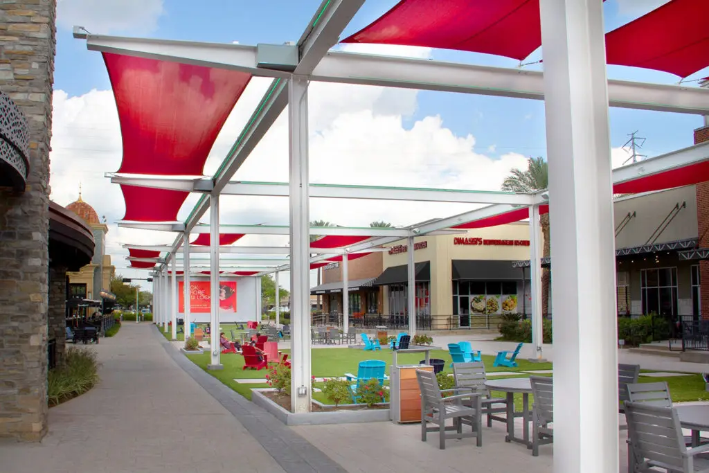 Shade structure at The Lawn at First Colony Mall with red tensile canopies, Adirondack chairs on turf, and restaurant fronts beyond