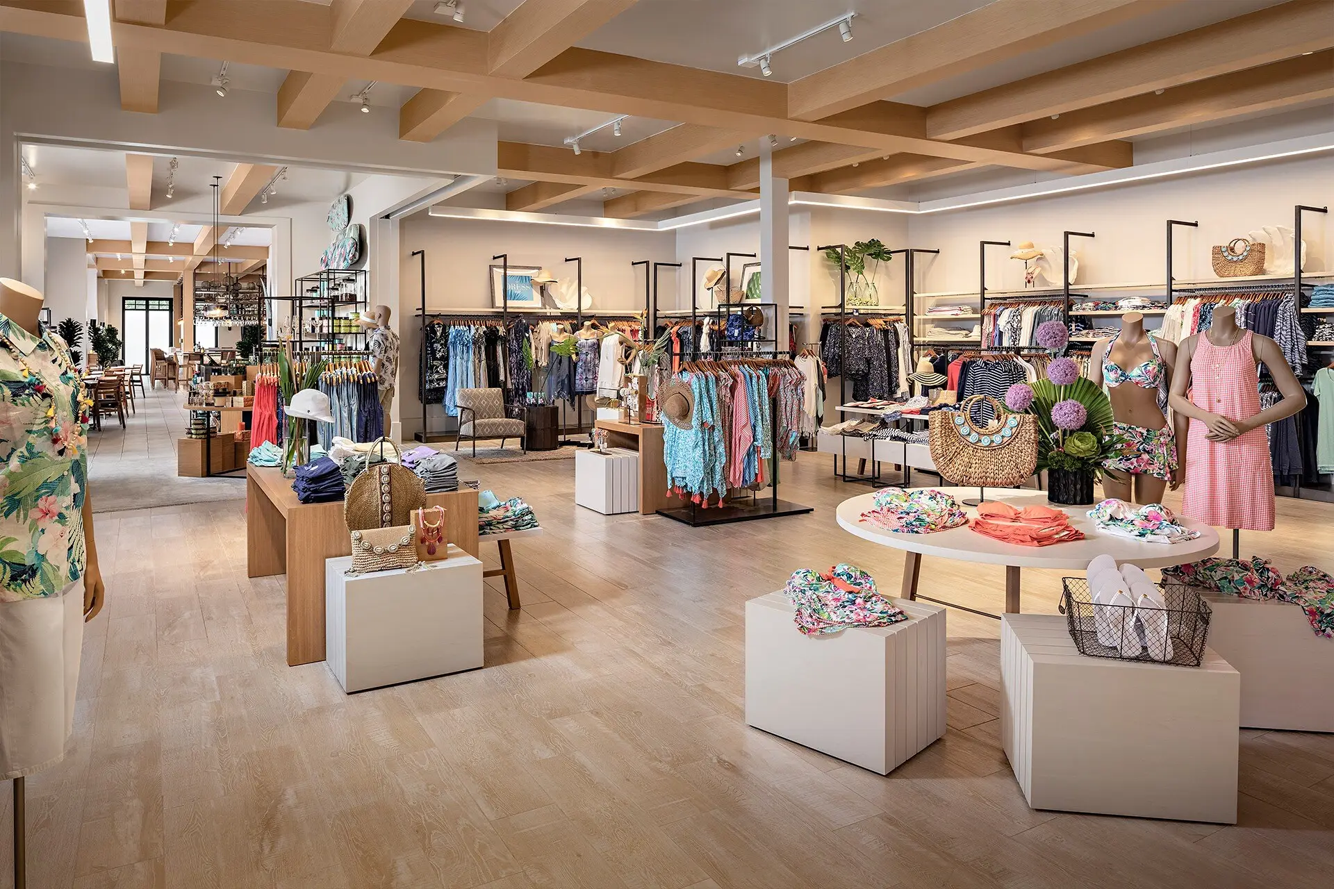Apparel floor at Tommy Bahama Newport Beach with wood beams, light oak flooring, clothing racks, and mannequins in tropical prints