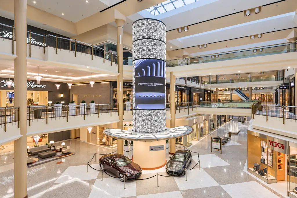Atrium at Tysons Galleria with a patterned digital column, two displayed Maseratis, and luxury storefronts on multiple levels