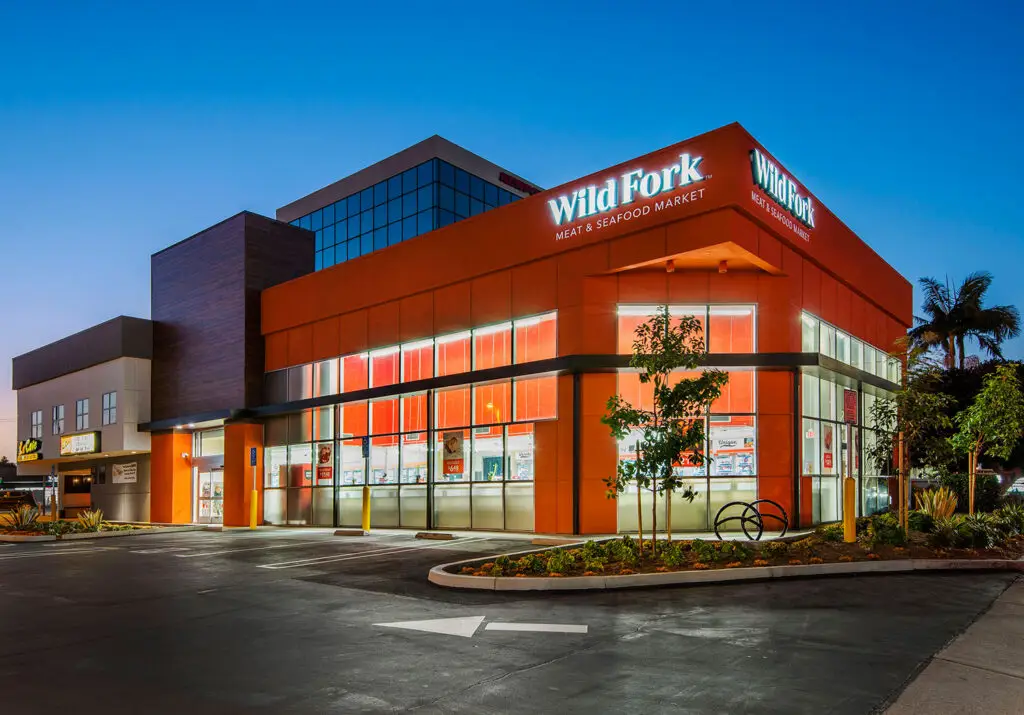 Wild Fork Costa Mesa storefront at dusk, with orange facade, corner glass, and Meat & Seafood Market signage