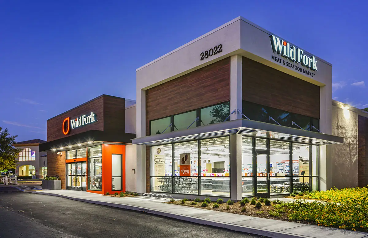 Dusk corner storefront of Wild Fork Laguna Niguel at 28022, with wood paneling, orange entry, and Meat & Seafood Market signage